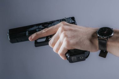 Beyaz tişörtlü bir adamın tabancasını kaldırırken ve silahı odaklanmış bir şekilde tutarken yakın plan fotoğrafı. Arkaplan tarafsız, kopyalama alanı sağlıyor.