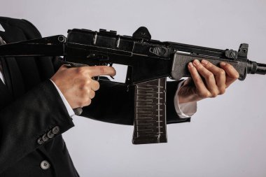 Siyah bir makineli tüfeğin ön sapını kavrayan bir elin yakın çekimi silahın vücudunun detaylarını gösteriyor. Görüntünün minimalist bir arka planı var, kopyalama alanı sağlıyor. Görünür bir logo yok.