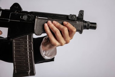 Siyah bir makineli tüfeğin ön sapını kavrayan bir elin yakın çekimi silahın vücudunun detaylarını gösteriyor. Görüntünün minimalist bir arka planı var, kopyalama alanı sağlıyor. Görünür bir logo yok.