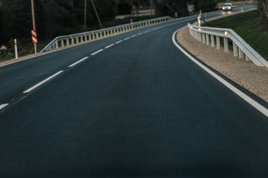 Pürüzsüz, boş bir yol bir tarafında sık ağaçlar, diğer tarafında açık alanlar olan ormanlık bir alanda esiyor. Yumuşak akşam ışığı, gökyüzünde ve üzerinde bolca fotokopi alanı olan huzurlu bir atmosfer yaratır.