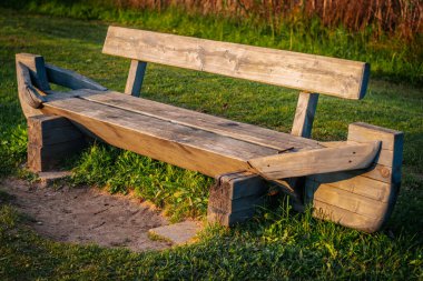 Kaba yontulmuş ahşaptan yapılmış kırsal bir ahşap bank ağaçların gölgelediği çimenli bir park alanında oturur. Yedek kulübesinde, doğal ortamında çekiciliğini arttıran tekne benzeri uçlar var..
