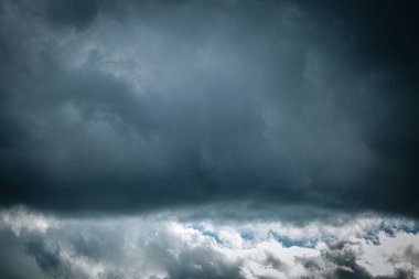 Tepemizde kara fırtına bulutları ve mavi gökyüzü olan dramatik bir gökyüzü. Karanlık ve aydınlık alanlar arasındaki zıtlık atmosfer ve yoğun bir atmosfer yaratır..