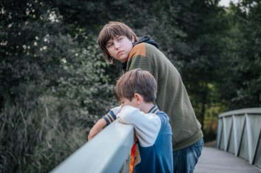 Genç bir çocuk ve bir genç bir köprünün korkuluklarına yaslanmış, dalgın ifadelerle uzaklara bakıyorlardı. Doğayla iç içe olan sahne, sessizliği yakalar..