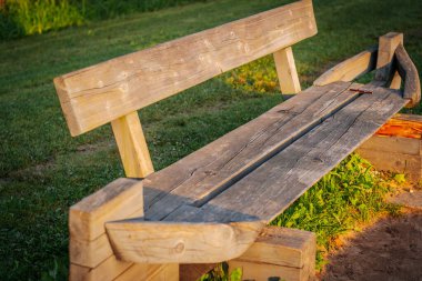 Kaba yontulmuş ahşaptan yapılmış kırsal bir ahşap bank ağaçların gölgelediği çimenli bir park alanında oturur. Yedek kulübesinde, doğal ortamında çekiciliğini arttıran tekne benzeri uçlar var..