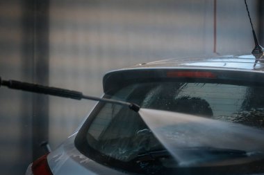 Bir arabanın arka camına su püskürten, yüzeyi etkin bir şekilde temizleyen bir elektrikli makinenin yakın çekimi. Su jetine ve araba camına odaklanmak için arka plan bulanık..