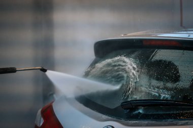 Bir arabanın arka camına su püskürten, yüzeyi etkin bir şekilde temizleyen bir elektrikli makinenin yakın çekimi. Su jetine ve araba camına odaklanmak için arka plan bulanık..