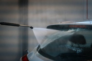 Bir arabanın arka camına su püskürten, yüzeyi etkin bir şekilde temizleyen bir elektrikli makinenin yakın çekimi. Su jetine ve araba camına odaklanmak için arka plan bulanık..