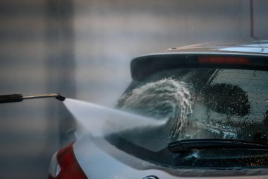 Bir arabanın arka camına su püskürten, yüzeyi etkin bir şekilde temizleyen bir elektrikli makinenin yakın çekimi. Su jetine ve araba camına odaklanmak için arka plan bulanık..