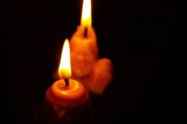 İki mum, arka planda hafif, yanıp sönen alevlerle parıldıyor. Balmumu hafifçe erimiş, sıcak ve huzurlu bir parıltı yaratmış. Görüntü huzurlu bir görüntü yakalar..