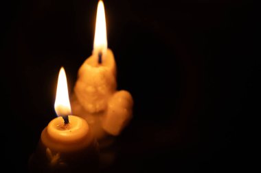 İki mum, arka planda hafif, yanıp sönen alevlerle parıldıyor. Balmumu hafifçe erimiş, sıcak ve huzurlu bir parıltı yaratmış. Görüntü huzurlu bir görüntü yakalar..