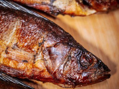 Ahşap bir yüzey üzerinde kurumuş kahverengi derili, kurutulmuş hamamböceğinin detaylı bir görüntüsü. Balığın pulları ve dokusu canlı bir şekilde vurgulanmış, kavrulmuş halini gösteriyor..