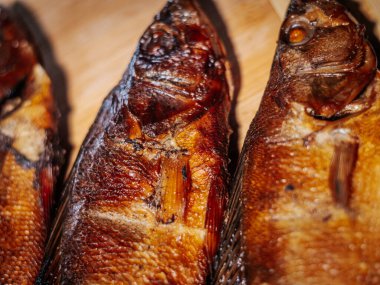 Ahşap bir yüzey üzerinde kurumuş kahverengi derili, kurutulmuş hamamböceğinin detaylı bir görüntüsü. Balığın pulları ve dokusu canlı bir şekilde vurgulanmış, kavrulmuş halini gösteriyor..