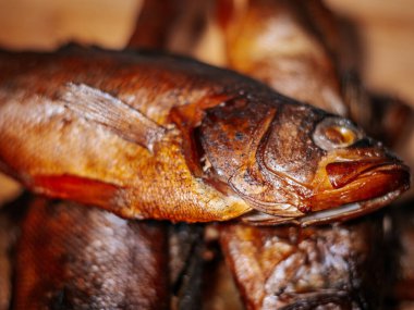 Zengin bir altın kahverengi deriye sahip füme balık yığını ahşap bir yüzey üzerinde düzenlenir. Doku ve duman hazırlığı ayrıntılı olarak vurgulanmıştır, mutfak temaları için idealdir.