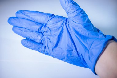 Avuç içi açık, arka planda açık mavi, tek kullanımlık nitril eldiven giyen bir elin yakın çekimi. Eldivenin dokusu ve ayrıntıları görünür..