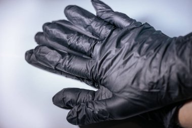 Siyah tek kullanımlık eldivenler giyen iki elin yakın plan çekimi, hafif arka planda bir araya getirilmiş. Eldivenlerin dokusu ve ayrıntıları görünür..