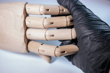 Siyah eldivenli bir elin ahşap bir el modelini tutarken yakın çekimi, düz, doğal ahşap ve sentetik eldiven malzemesi arasındaki kontrastı gösteriyor. Hafif bir arkaplana göre ayarla.