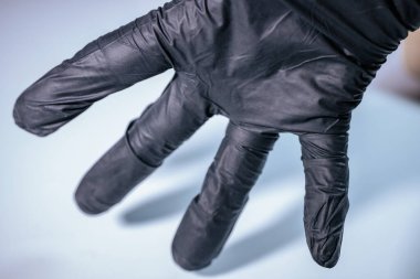 Siyah tek kullanımlık eldiven yakın plan, pürüzsüz ve esnek materyali vurguluyor. Eldiven kısmen hafif bir arka plana doğru çekilir ve koruyucu ve işlevsel tasarımı vurgulanır..