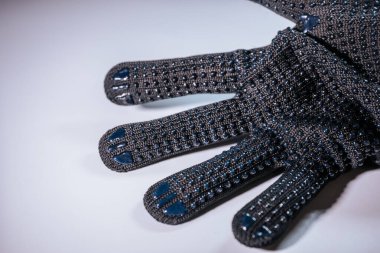 Siyah örgü eldivenin detaylı bir görüntüsü, kumaş dokusunu ve uzatılmış parmaklarını vurguluyor. Eldiven hafif bir arkaplana dayanır ve minimalist bir kompozisyon oluşturur..