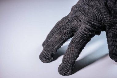 Siyah örgü eldivenin detaylı bir görüntüsü, kumaş dokusunu ve uzatılmış parmaklarını vurguluyor. Eldiven hafif bir arkaplana dayanır ve minimalist bir kompozisyon oluşturur..