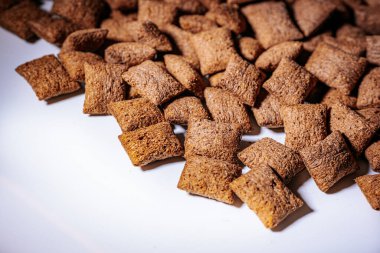 Beyaz bir yüzeye dağılmış gevrek kahverengi mısır gevreği yığını, dokularını ve doğal görünümlerini ön plana çıkarıyor..