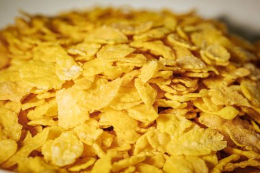 Altın mısır gevreğiyle dolu beyaz bir kase gevrek dokusunu ve parlak sarı rengini gözler önüne seriyor..