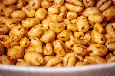 Beyaz bir kâseyi dolduran parlak bir bal kaplamalı altın renkli mısır gevreği parçaları..