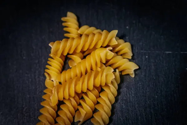 Koyu bir arkaplan üzerine dizilmiş, pişirilmemiş sarı rotini makarna sarmalı, kıvrımlarını ve basit, sade cazibelerini gözler önüne seriyor..