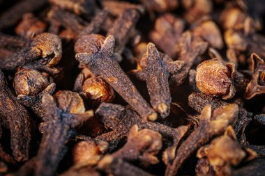 Kurumuş karanfillerin aşırı yakın çekimi, dokularının ve yapılarının karmaşık detaylarını gösteriyor. Zengin kahverengi tonlar sıcak ışıkla vurgulanır..