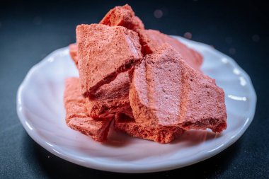 Beyaz bir tabağa dizilmiş yumuşak, pembemsi atıştırmalık külçeler koyu bir arka plana karşı, dokularını ve pastel tonlarını renklendiriyor. Atıştırmalık ya da tatlı teması için mükemmel.