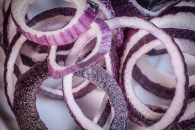 Arkaplan yüzeyine dizilmiş mor soğan halkalarının detaylı bir yakın çekimi, dokularını ve canlı renklerini vurguluyor..