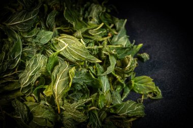 Koyu arkaplanda kurumuş yeşil nane yapraklarının desenli yakın çekimi, karmaşık damarları ve doğal desenleri vurguluyor..