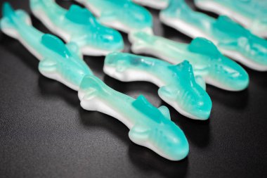 Siyah arkaplandaki mavi ve beyaz şekerleme yığınının yakın çekimi. Şekerlerin parlak, şeffaf bir dokusu ve yumuşak, çiğnenebilir bir görüntüsü var..