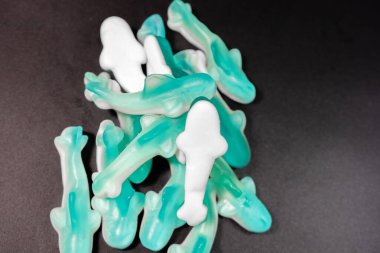 Siyah arkaplandaki mavi ve beyaz şekerleme yığınının yakın çekimi. Şekerlerin parlak, şeffaf bir dokusu ve yumuşak, çiğnenebilir bir görüntüsü var..