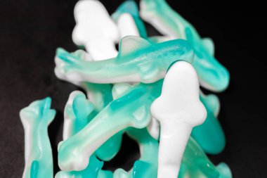 Siyah arkaplandaki mavi ve beyaz şekerleme yığınının yakın çekimi. Şekerlerin parlak, şeffaf bir dokusu ve yumuşak, çiğnenebilir bir görüntüsü var..