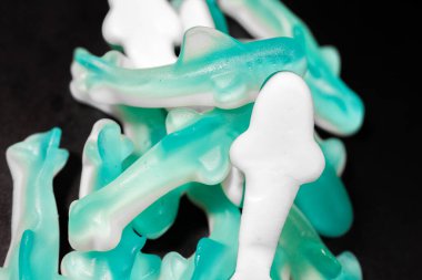 Siyah arkaplandaki mavi ve beyaz şekerleme yığınının yakın çekimi. Şekerlerin parlak, şeffaf bir dokusu ve yumuşak, çiğnenebilir bir görüntüsü var..