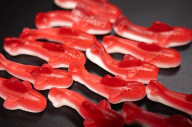 Siyah bir yüzeye yerleştirilmiş beyaz tabanlı bir kaç kırmızı şekerleme. Şekerlerin parlak, şeffaf bir dokusu ve yumuşak, çiğnenebilir bir görüntüsü var..