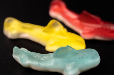 Kırmızı, sarı, mavi ve beyaz şekerlemeli çok renkli köpekbalığı şekerlemeleri. Şekerlerin parlak, şeffaf bir dokusu vardır ve bir araya toplanarak canlı bir görüntü oluştururlar..