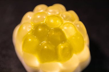 Engebeli, şeffaf yüzeyi meyve ya da hücrelere benzeyen parlak sarı şekerlerden oluşan bir makro çekim. Parlak dokuları, koyu bir arkaplan ile çelişiyor..