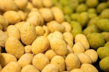 Biri yeşil baharatlı, diğeri de sarı kaplamalı olmak üzere iki çeşit fıstığın detaylı bir yakın çekimi. Zıt renkler ve dokular bu çıtır çıtır atıştırmalığı vurgular.