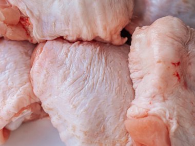 Derisi yüzülmüş, beyaz bir tabağa yerleştirilmiş taze çiğ tavuk butlarının yakın çekimi. Ayrıntılı doku ve doğal renk etin kalitesini vurguluyor, pişirilmeye hazır..