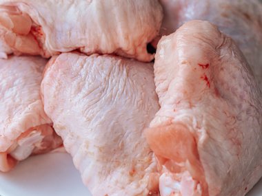 Derisi yüzülmüş, beyaz bir tabağa yerleştirilmiş taze çiğ tavuk butlarının yakın çekimi. Ayrıntılı doku ve doğal renk etin kalitesini vurguluyor, pişirilmeye hazır..