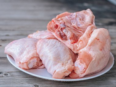 Derisi yüzülmüş, beyaz bir tabağa yerleştirilmiş taze çiğ tavuk butlarının yakın çekimi. Ayrıntılı doku ve doğal renk etin kalitesini vurguluyor, pişirilmeye hazır..