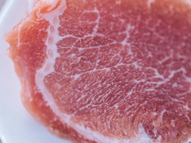 Beyaz bir tabağa konmuş taze, çiğ domuz pirzolası. Zengin doku ve doğal renk etin kalitesini vurgular, pişirilmeye hazır..