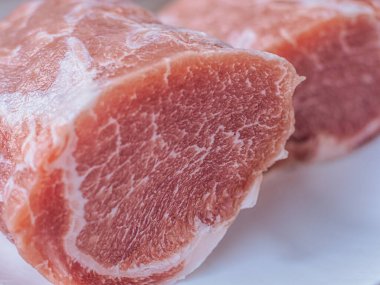 Beyaz bir tabağa konmuş taze, çiğ domuz pirzolası. Zengin doku ve doğal renk etin kalitesini vurgular, pişirilmeye hazır..