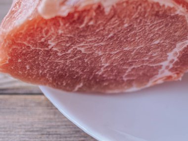 Beyaz bir tabağa konmuş taze, çiğ domuz pirzolası. Zengin doku ve doğal renk etin kalitesini vurgular, pişirilmeye hazır..