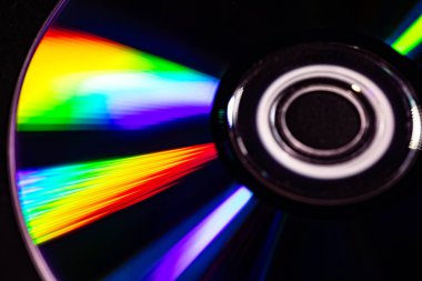 Parlak gökkuşağı yansımalı bir CD 'nin yakın çekimi. Dinamik bulanık etki, karanlık bir arka plana karşı soyut ve fütüristik hissi artırır..