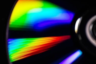 Parlak gökkuşağı yansımalı bir CD 'nin yakın çekimi. Dinamik bulanık etki, karanlık bir arka plana karşı soyut ve fütüristik hissi artırır..