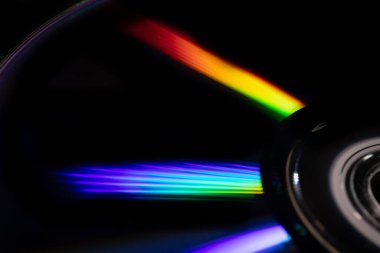 Parlak gökkuşağı yansımalı bir CD 'nin yakın çekimi. Dinamik bulanık etki, karanlık bir arka plana karşı soyut ve fütüristik hissi artırır..