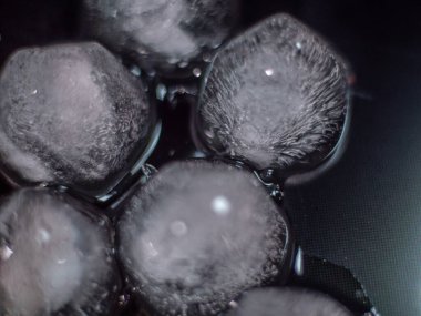 Donmuş iç dokuları ve buz parçalarını koyu bir arkaplanda gösteren yakın çekim bir buz küpü. Soyut ve görsel olarak çarpıcı.