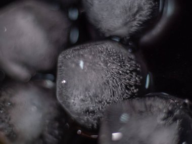 Donmuş iç dokuları ve buz parçalarını koyu bir arkaplanda gösteren yakın çekim bir buz küpü. Soyut ve görsel olarak çarpıcı.